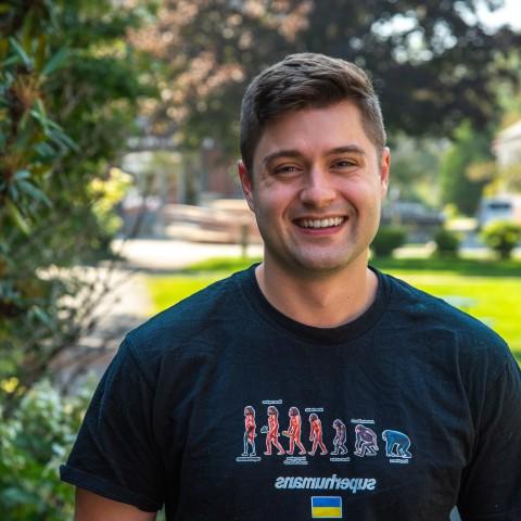 罗伯特·莫特利在全球网络赌博平台帕克馆外的院子里摆姿势拍照. He wears a shirt that reads "Superhumans," which is the name of the clinic he volunteered at in Ukraine.